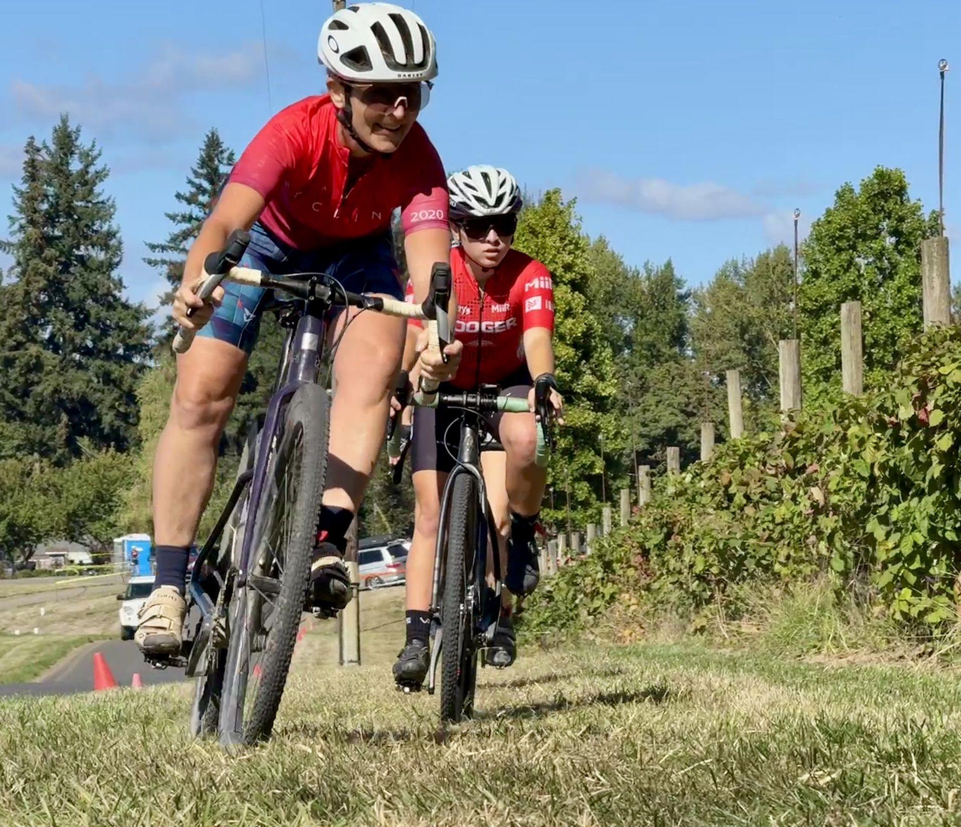 Two riders in red jerseys race along the grassy course.